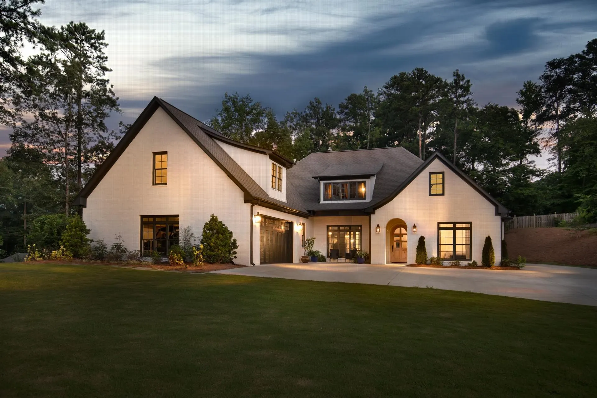 White brick custom home at dusk with warm lights in the windows